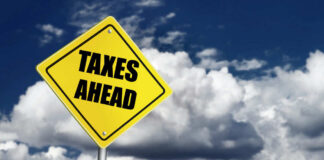 Yellow road sign reading taxes ahead clouds background