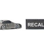 A miniature gray sports car next to a black sign that reads 'RECALL'