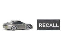 A miniature gray sports car next to a black sign that reads 'RECALL'