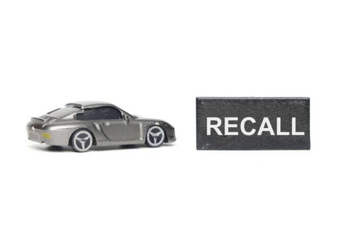 A miniature gray sports car next to a black sign that reads 'RECALL'