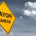 Yellow warning sign indicating layoffs ahead against a cloudy background