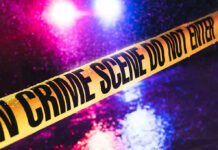 Crime scene tape with flashing lights in background.