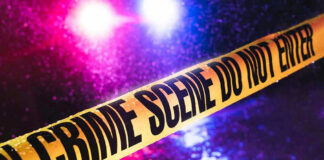 Crime scene tape with flashing lights in background.