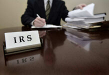 IRS sign on desk, person handling paperwork behind.