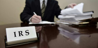 IRS sign on desk, person handling paperwork behind.