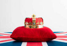 A royal crown resting on a red velvet pillow with a British flag background