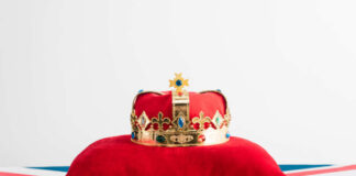 A royal crown resting on a red velvet pillow with a British flag background