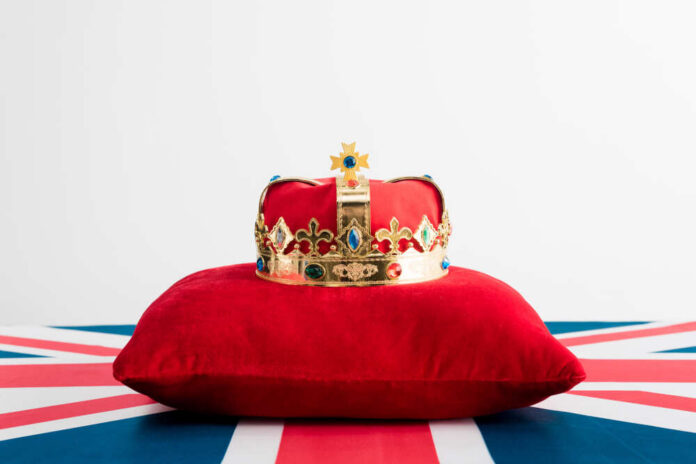 A royal crown resting on a red velvet pillow with a British flag background