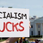 Person holding a protest sign that reads 'SOCIALISM SUCKS' in front of the White House
