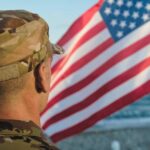 Soldier in uniform standing in front of an American flag by the ocean
