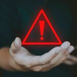 A hand holding a red warning triangle with an exclamation mark