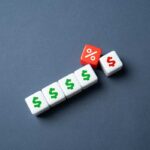 White dice with dollar signs and a red dice with a percentage symbol on a gray background