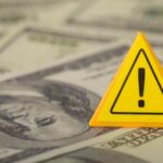 A yellow warning sign placed on a background of dollar bills