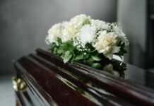 A floral arrangement of white roses and greenery on a polished casket