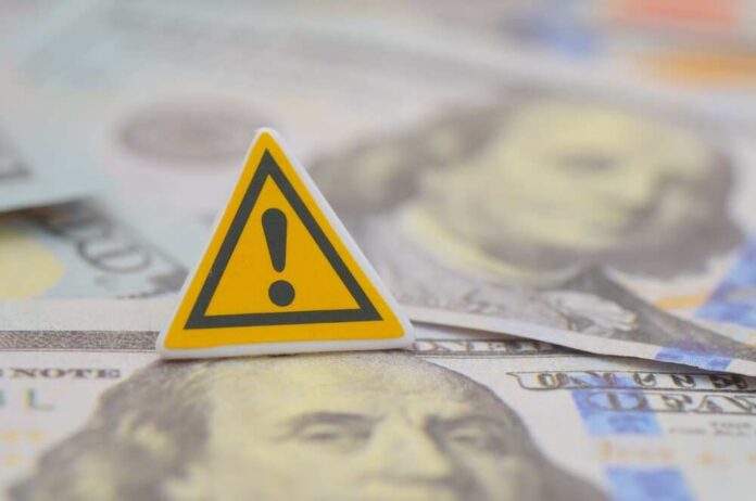 shutterstock_2733990965.jpg A warning sign placed on top of U.S. dollar bills