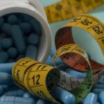 Blue capsules spilled from a white bottle alongside measuring tapes