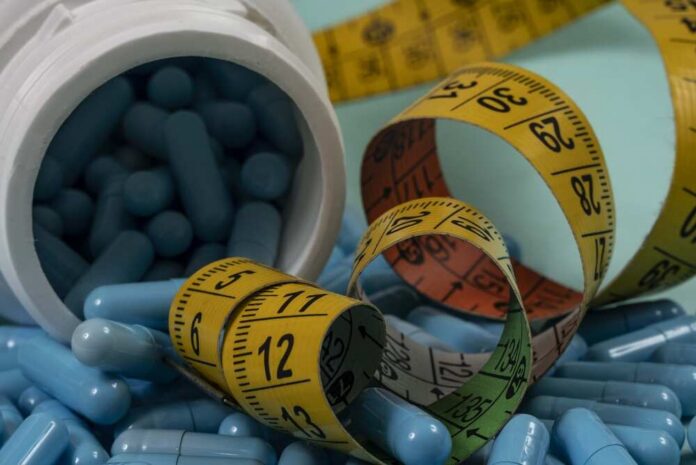 Blue capsules spilled from a white bottle alongside measuring tapes