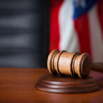 Trump’s Bold Blue Plan Sparks Lawsuit A wooden gavel resting on a sound block with an American flag in the background