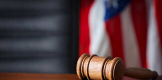 A wooden gavel resting on a sound block with an American flag in the background