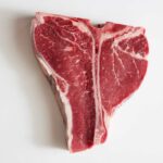 Memorial Day SHOCKER: Grocery Bills Sizzle! Raw T-bone steak on a white background