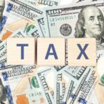 Wooden blocks spelling 'TAX' on a background of U.S. dollar bills