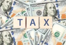 Wooden blocks spelling 'TAX' on a background of U.S. dollar bills