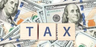 Wooden blocks spelling 'TAX' on a background of U.S. dollar bills