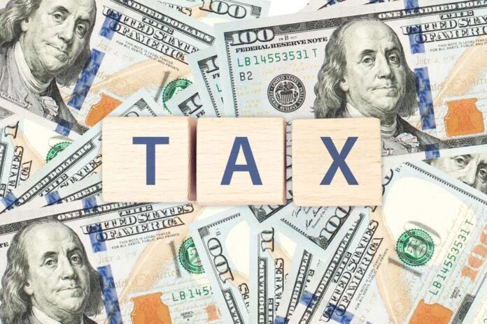 Wooden blocks spelling 'TAX' on a background of U.S. dollar bills
