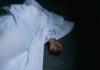 Hand emerging from under white sheet on dark surface.