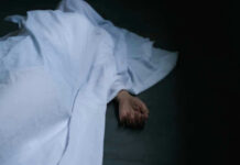 BOXCAR HORROR: Six Dead Hand emerging from under white sheet on dark surface.