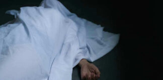 Hand emerging from under white sheet on dark surface.