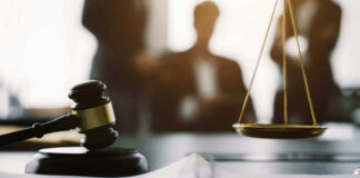 Gavel and scales in courtroom with blurred figures behind.