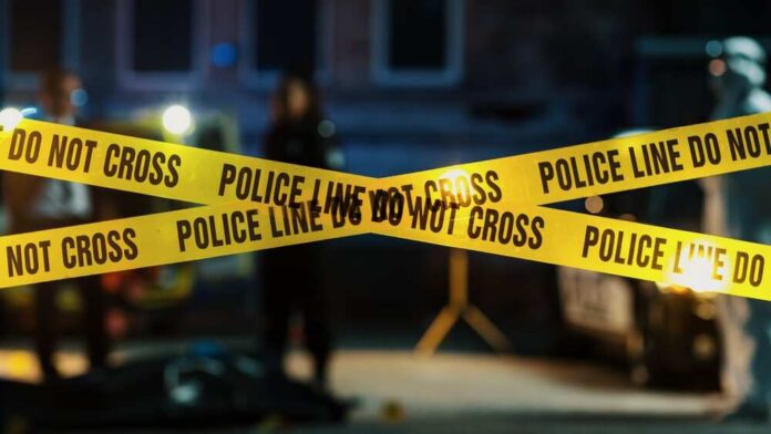 Police tape marking a crime scene with blurred figures in the background