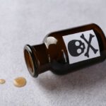 Amber glass bottle labeled with a skull and crossbones, tipped over with liquid spilled