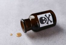 Amber glass bottle labeled with a skull and crossbones, tipped over with liquid spilled