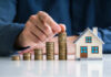 Mortgage Math Just Torched First-Time Buyers Hand stacking coins beside a miniature house model.