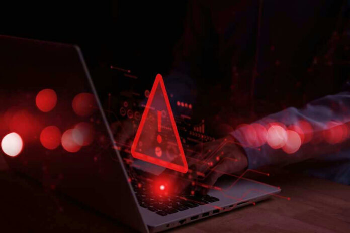 shutterstock_2248466625 Warning symbol over laptop with user.