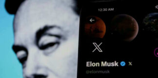Elon Musks profile on mobile screen, blurred background face.