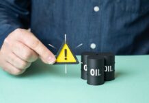 Oil Shock Warning: $160 Barrel Looms A person holding a warning sign next to oil barrels
