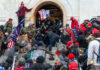 Crowd storming entrance of a government building with flags.