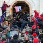 Capitol Riot Loophole Slams Shut Crowd storming entrance of a government building with flags.