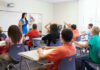 Teacher instructing students raising hands in a classroom.
