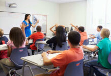 Teacher instructing students raising hands in a classroom.