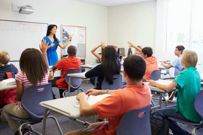 shutterstock_199144970 Teacher instructing students raising hands in a classroom.