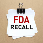 Baby Products Recalled — Plastic Inside? A notice labeled 'FDA RECALL' clipped to white papers on a brown background