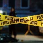 VIDEO: Ambush Leaves Cop, Family Dead Police tape marking a crime scene with blurred figures in the background