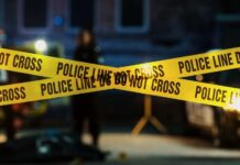 VIDEO: Ambush Leaves Cop, Family Dead Police tape marking a crime scene with blurred figures in the background