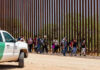 Group of people walking by a border fence.