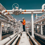 Worker in orange jacket inspecting industrial pipes.