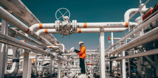 Worker in orange jacket inspecting industrial pipes.